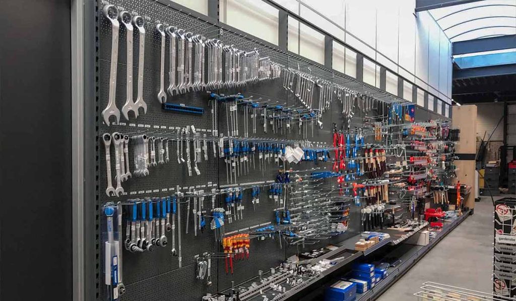 Grote grijze stellingwand in een winkel gevuld met ordelijk uitgestalde handgereedschap zoals sleutels, schroevendraaiers en ander gereedschap in blauw en rood.