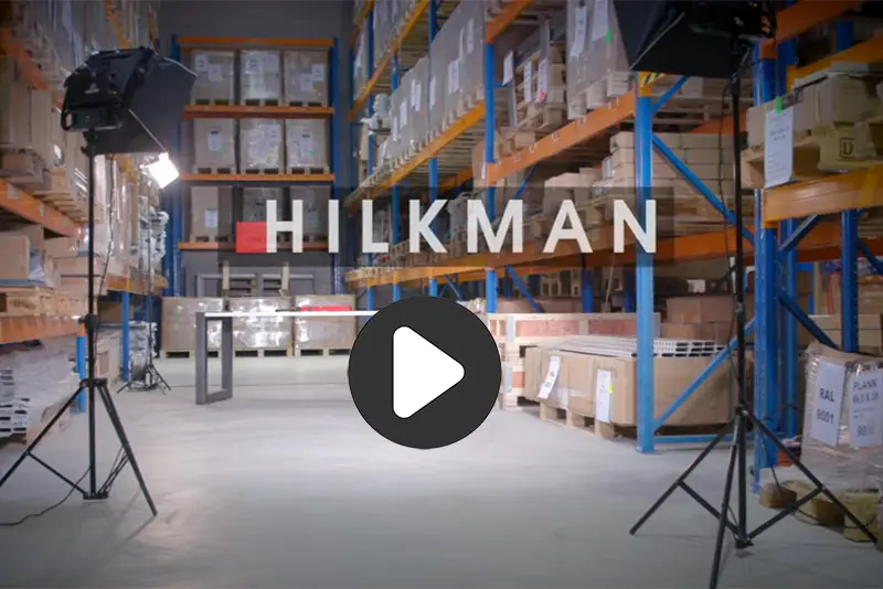 Industrieel magazijn met oranje en blauwe stellingen, kartonnen dozen en professionele verlichting voor een video-opname.