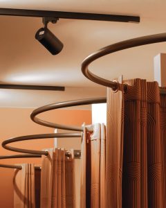 Moderne winkelruimte met bronze-kleurige gordijnrails en spotlights tegen een beige muur.