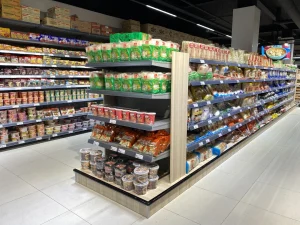 Supermarktafdeling met metalen stellingen gevuld met verpakte voedselproducten, noodles, sauzen en ingrediënten in een moderne winkel.