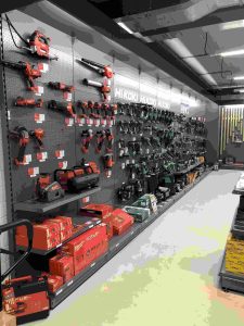Grote wandstellage in gereedschapwinkel met rode en zwarte elektrische gereedschappen, opslag en displaykasten onder fluorescente verlichting.