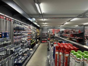 Gereedschappenwinkel met metalen wandstellingen vol gereedschap, werktuigen en chemicaliën in rode en blauwe verpakkingen.