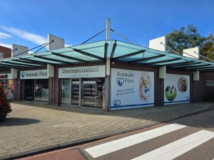 Dierenspeciaalzaak met glazen afdak, bakstenen gevel, vitrinepuien met dierenfoto's en betonnen terrasvloer aan de straat.