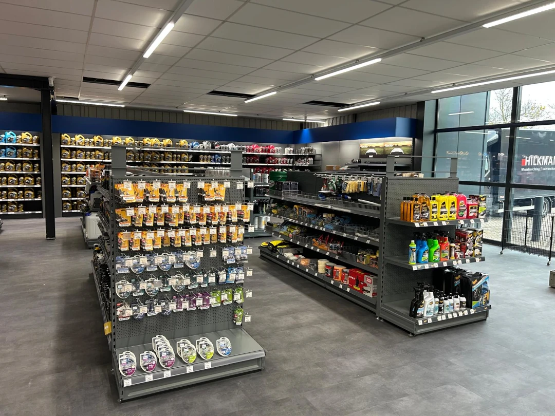 Moderne winkelruimte met metalen stellingen vol verfproducten, fluorescerende verlichting en grote ramen aan de zijkant.