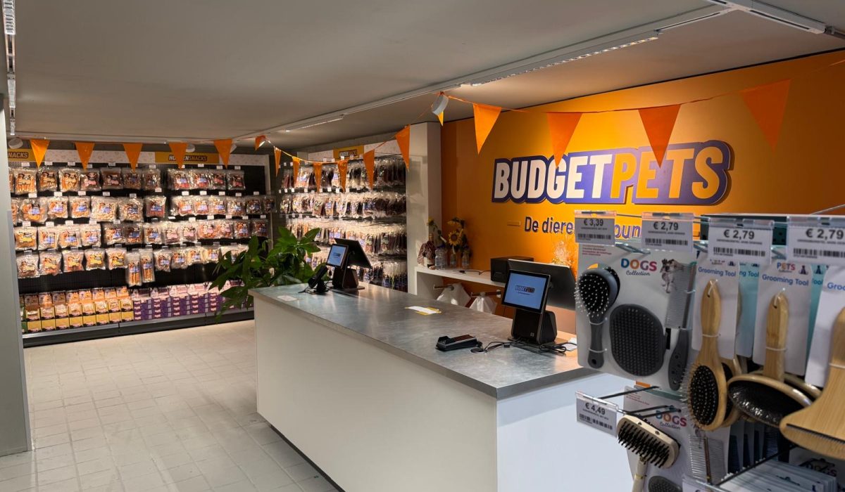 Interieur van een dierenwinkel met oranje decoratie, verkoosbalie met kassa's, stellingen met diervoeding en verzorgingsproducten.