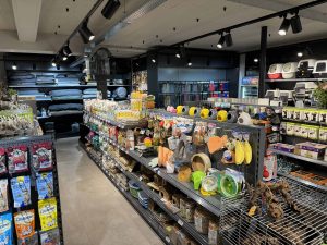 Moderne dierenwinkel met zwarte stellingen vol dierbenodigdheden, voer, speelgoed en accessoires onder helder LED-verlichting.
