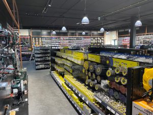 Groot gereedschapswerktuigenmagazijn met gele en zwarte stellingen vol met verschillende gereedschappen, onderdelen en accessoires onder pendellamp verlichting.