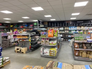 Interieur van een dierenvoerwinkel met metalen stellingen vol voederpakketten, bedden en accessoires onder LED-verlichting.