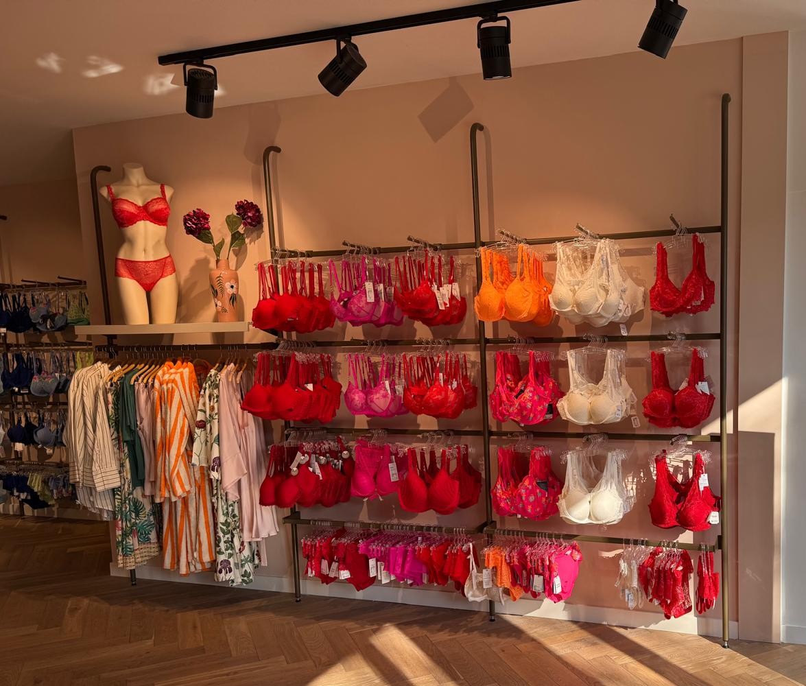 Lingerie winkel met metalen stellingen vol rode en roze ondergoed, mannequin in etalage en kledingrekken met diverse kledingstukken.