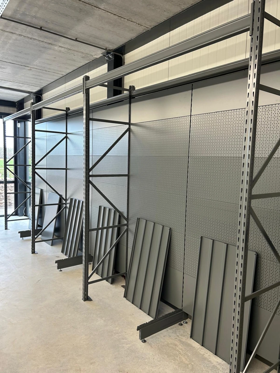 Industriële showroom met zwarte metalen stellingkasten, grijze pegboard panelen en grijze verticale displays op wieltjes onder betonnen plafond.