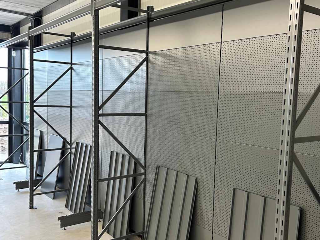 Industrieel ingerichte showroom met zwarte metalen stellingen, gaasdeuren en grijze geperforeerde wandpanelen.