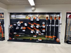 Winkeluitstalling met zwarte stellingwand waarop diverse oranje en zwarte tuingereedschappen, kettingzagen en accu's voor professionals zijn uitgesteld.