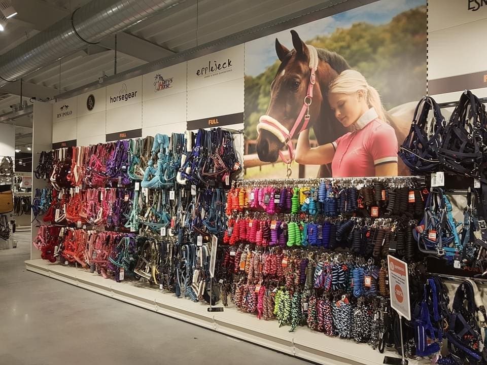Winkelstandaard met gekleurde paardenbegels en zadels, ondersteund door een grote foto van een meisje met een paard bovenaan.
