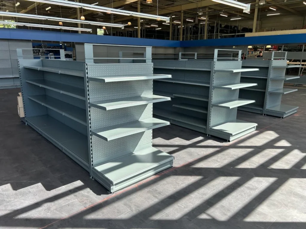 Lege winkelstellingen met witte en grijze metalen planken in een grote winkelruimte met betonnen vloer.