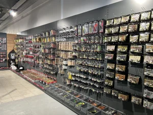 Een uitgebreid assortiment gereedschap en bouwmaterialen uitgestald op zwarte metalen stellingen en pegboards in een professionele winkel.