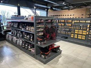 Winkelinterieur met zwarte metalen stellingen waarop gereedschap, accessoires en verpakte producten zijn uitgestald, inclusief rode koptelefoons en een werkbank.