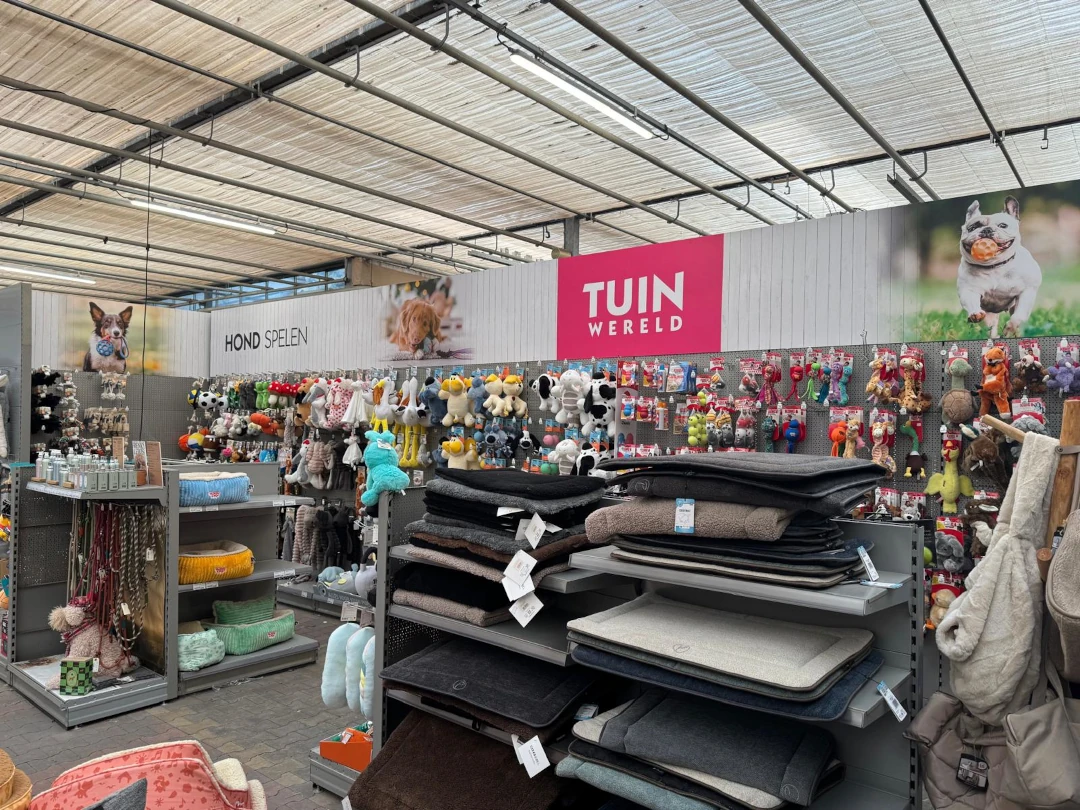 Een petwinkel met metalen stellingen vol dierenbenodigdheden, speelgoed, bedden en accessoires onder een industrieel plafond.