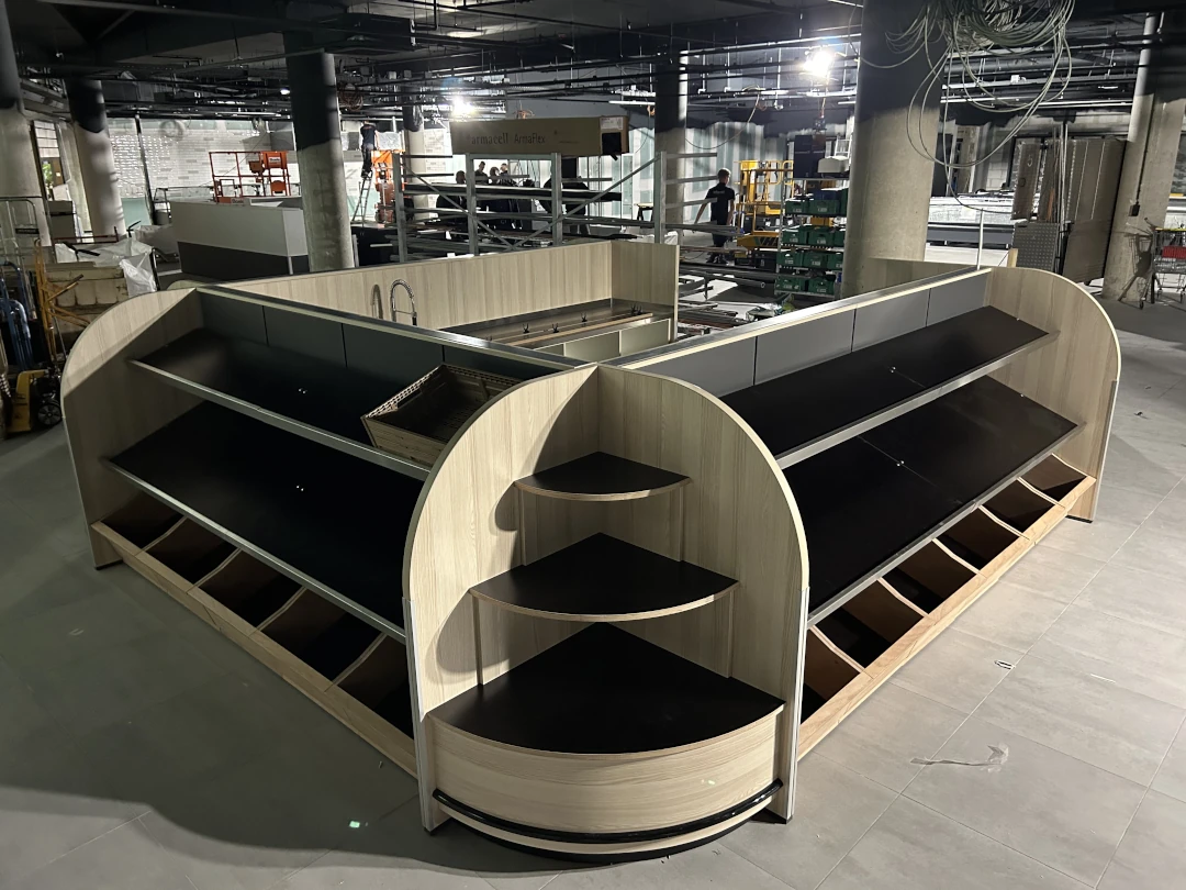 Moderne winkelbalies met houtlook en zwarte planken in een industrieel interieur met betonnen pilaren en werkplaats op de achtergrond.