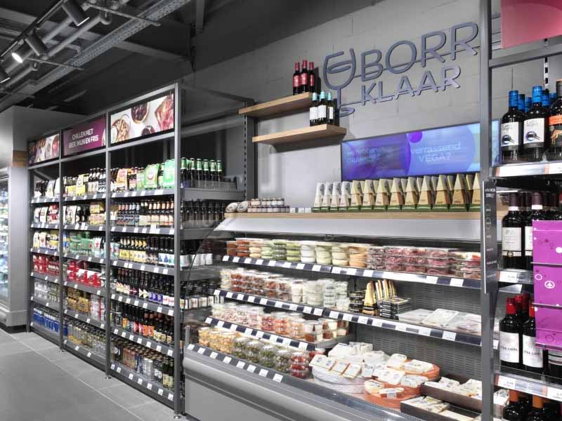Winkelhoek met gekoelde display en metalen stellingen vol verpakte voedingsproducten en dranken in een supermarkt.