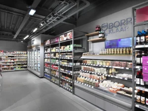 Moderne supermarktafdeling met gesloten en open koelkasten vol zuivelproducten, vleeswaren en andere verpakte goederen onder LED-verlichting.