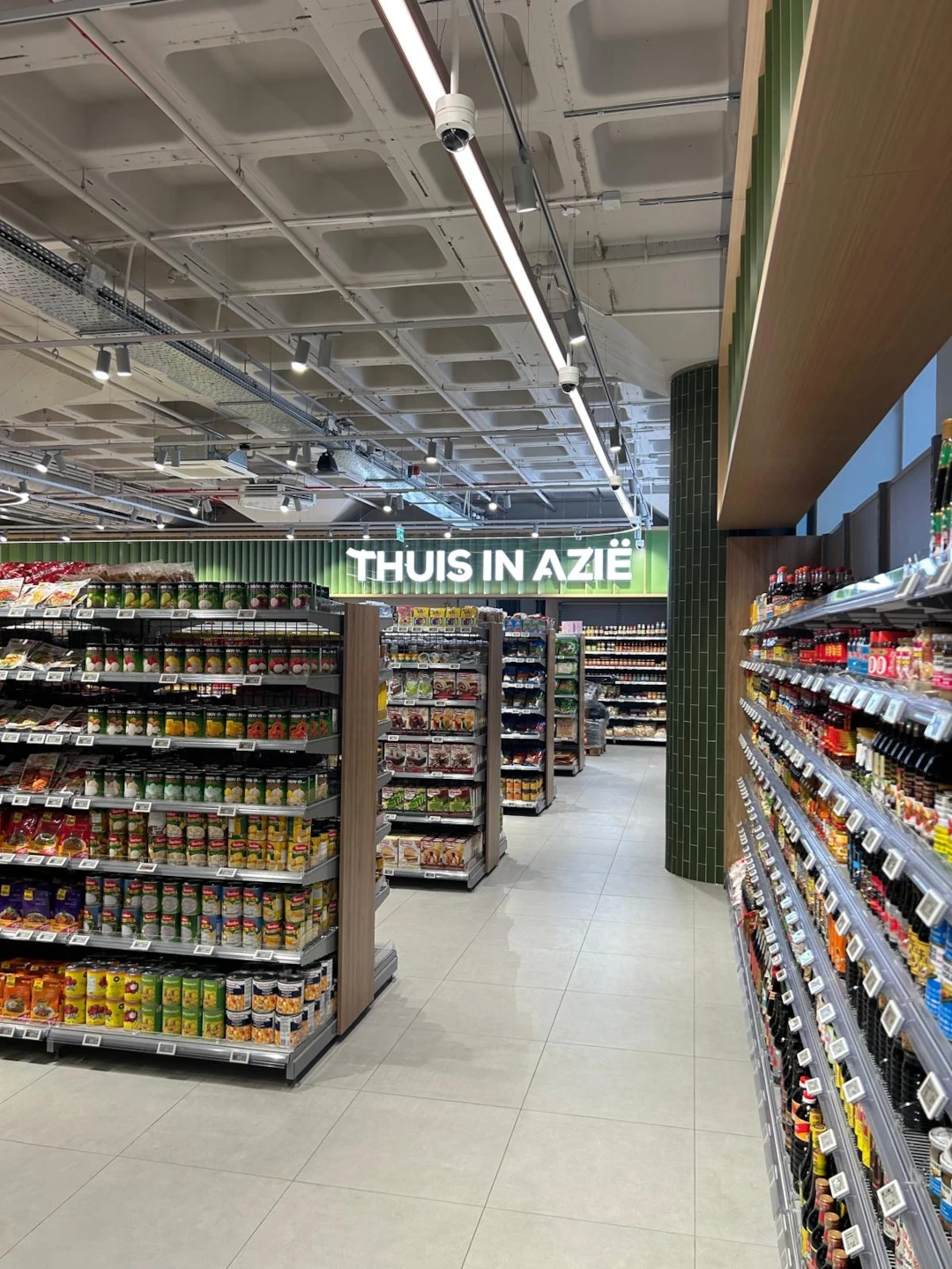 Een moderne supermarktgang met groene stellingen vol voedselproducten aan beide zijden en een verlicht plafond.
