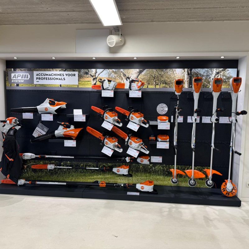 Winkeluitstalling met zwarte stellingwand waarop diverse oranje en zwarte tuingereedschappen, kettingzagen en accu's voor professionals zijn uitgesteld.